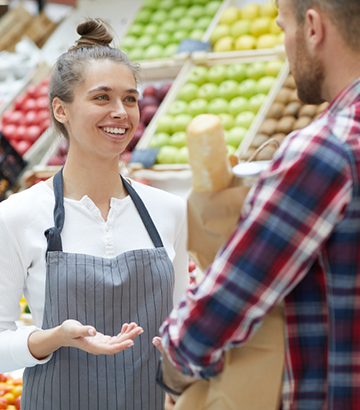 smiling grocery employee talking with male shopper holding grocery bag with bread